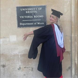 A young woman standing by a sign in graduation robes